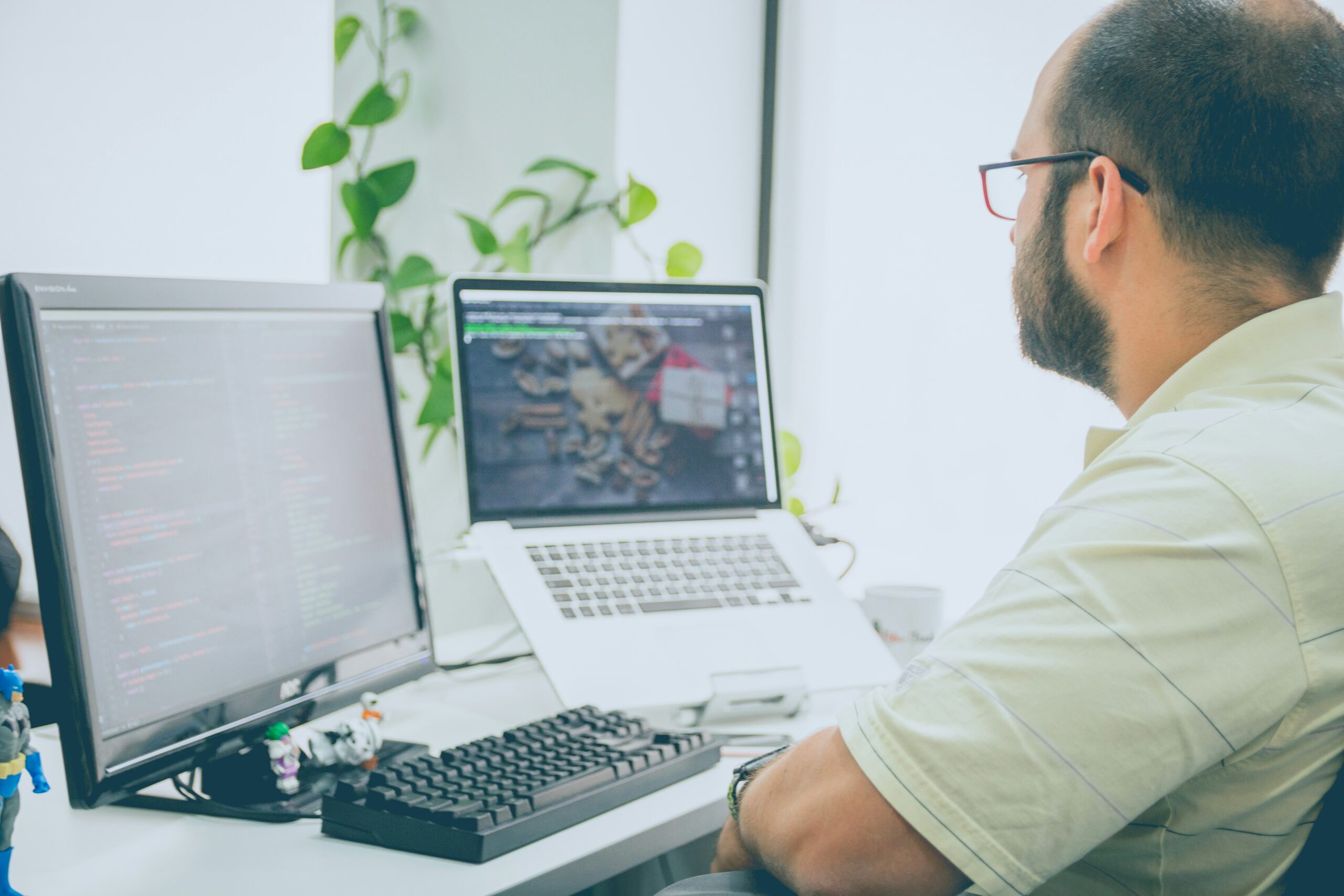 A man wearing glasses looking at a computer screen and a laptop.